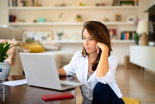 Thoughtful businesswoman using laptop at home