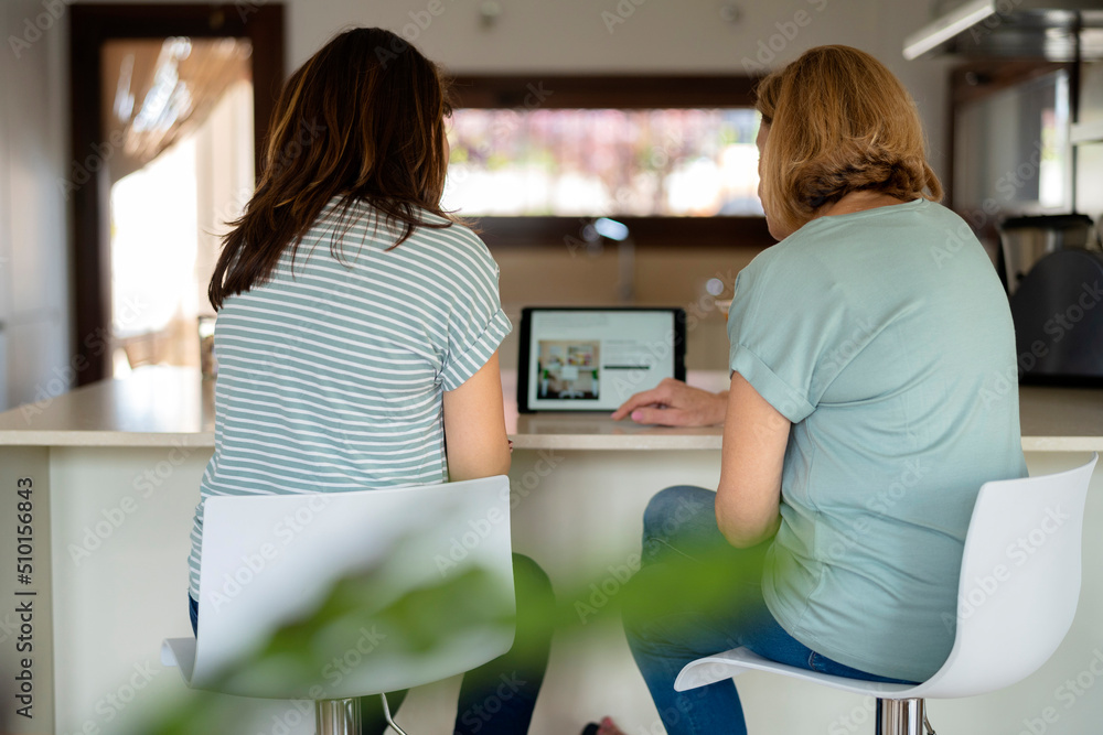 Unrecognizable women browsing tablet in kitchen Unrecognizable women browsing tablet in kitchen