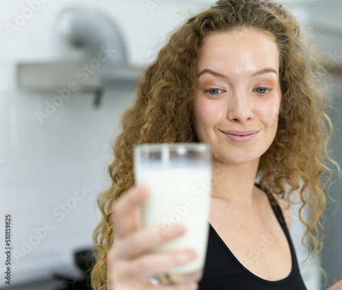close up face of beautiful healthy woman look at milk in glass in kitchen with copy space. beautiful caucasian woman cooking healthy diet fruit or vegetable in kitchen