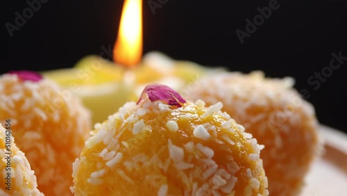 Close up of Indian sweet Motichoor Laddoo or Bundi Laddu. Coconut sweet Laddoo or Nariyal Ladduis on black background, blurry candle in the background, focus on a ladoo.