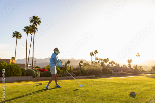 Backlit Senior Citizen Woman Playing Golf hits ball off tee  photo
