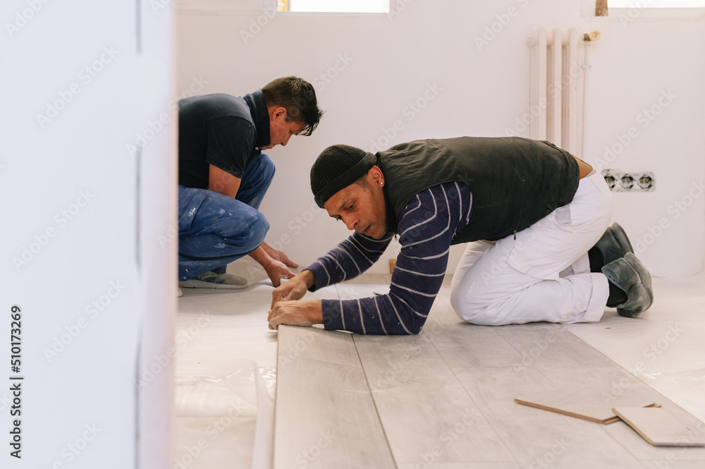 Male workers installing floor together Male workers installing floor together