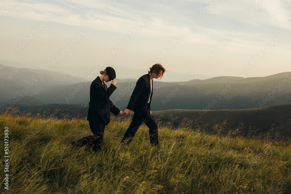 Stylish couple in black suits on a walk among mountain landscapes Stylish couple in black suits on a walk among mountain landscapes