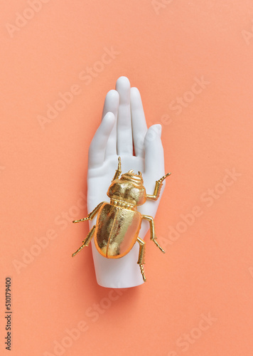 Plastic mannequin hand holds golden bug. photo