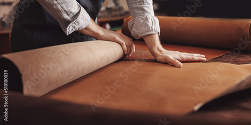 Cobbler working with skin textile in workshop. Tailor hold different rolls natural brown leather photo