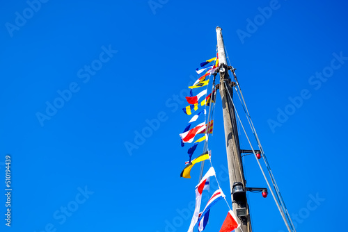 International code of signals flags flying in the wind on a mast of a sailboat with colorful maritime flags against a blue sky