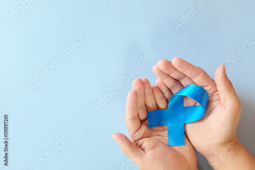 Top view of hands holding blue awareness ribbon. Prostate cancer, colon and colorectal cancer, peace, alopecia and arthritis care concept. photo