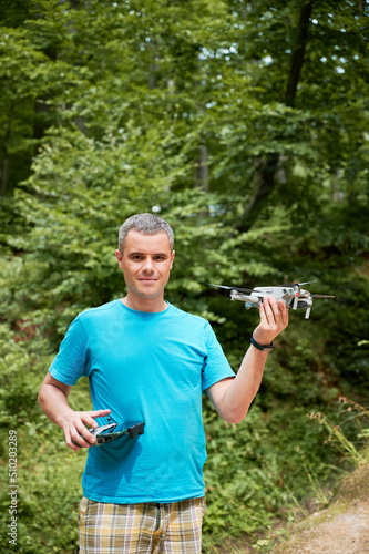 Man operating drone using remote controller. Man using drone for photos and video making while standing in green forest.