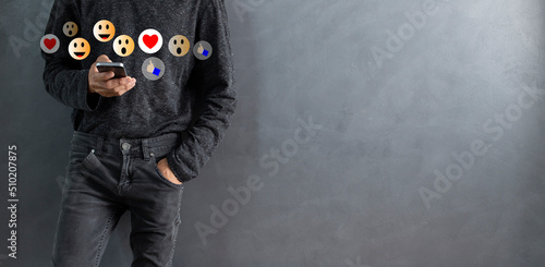 Social media concept with lifestyle young man using smartphone and pressing comment  icon  during watching  live while standing and gray wall  copy space background photo