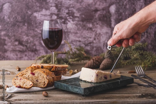 Wensleydale cheese with cranberries, red wine, honey, nuts, raisins on marble cutting board. Black concrete background. Selective focus.