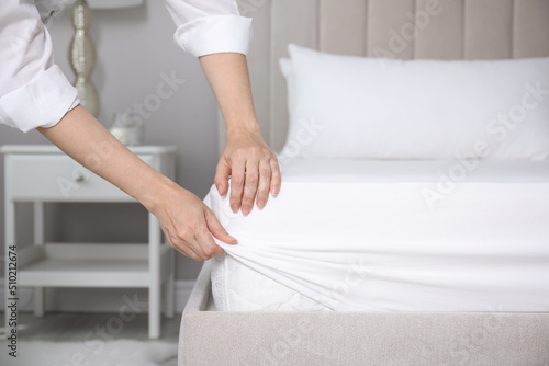 Woman putting white fitted sheet over mattress on bed indoors, closeup photo