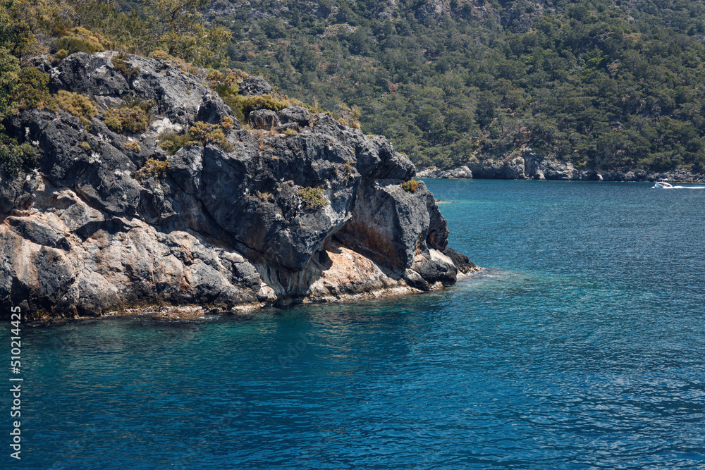 Beautiful seascape. Travel concept. Seascape on the background of the wild rocky coast. Wild beach, azure water and rocks. Luxury summer adventure, Aegean Sea, Turkey. Postcard view. Steep rocky shore