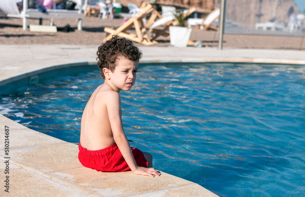 beautiful boy sitting at the edge of the pool