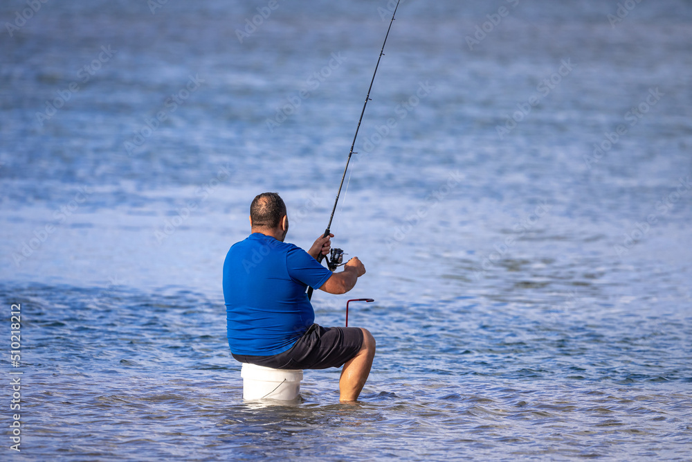 An unidentifiable middle aged man with a fishing rod sits on a