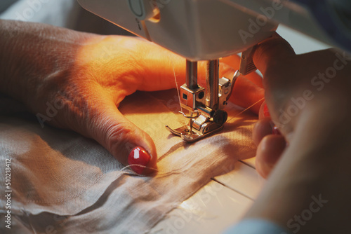 Fototapeta Naklejka Na Ścianę i Meble -  Photo of woman's hands in process of sewing linen dress using automatic sewing machine