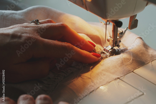 Photo of woman's hands in process of sewing linen dress using automatic sewing machine photo