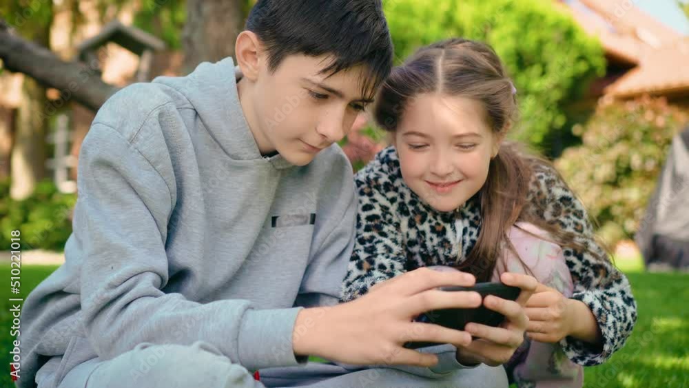 Cheerful kids boy and girl playing together in mobile games on smartphone in home yard. Concept of digitalization and modern technologies in children environment Cheerful kids boy and girl playing together in mobile games on smartphone in home yard. Concept of digitalization and modern technologies in children environment