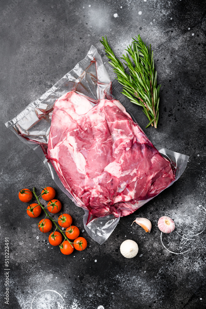 Fresh raw mutton shoulder meat, with ingredients and herbs, on black dark stone table background, top view flat lay