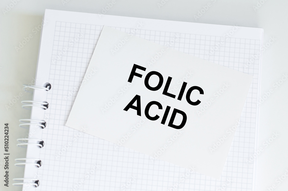 FOLIC ACID is the text on a card that sits on a notepad on a light desk. Medical concept FOLIC ACID is the text on a card that sits on a notepad on a light desk. Medical concept