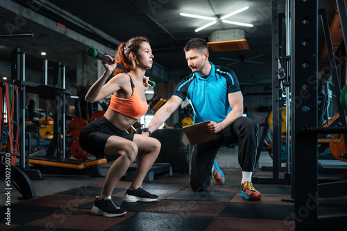 Obraz na płótnie young female workout and exercising barbell squat in gym with personal trainer