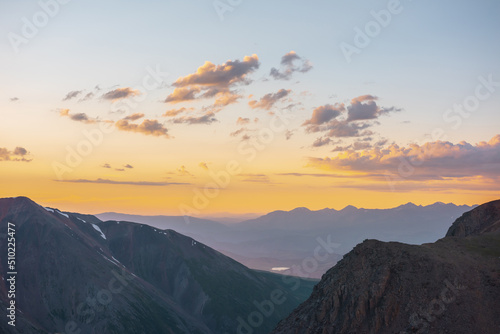 Atmospheric alpine landscape with large mountains in orange dawn sky. Colorful top view to high mountain range under cloudy sky in sunset colors. Awesome mountain sunset scenery at very high altitude.