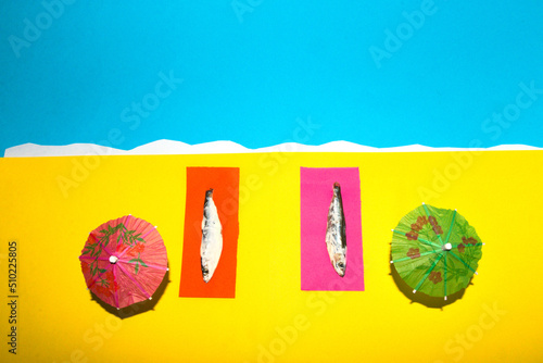 two fish sunbathing on the sandy beach  creative summer design  summer beach parasols  relax time  abstract background
