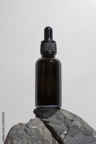 Black glass dropper bottle with a pipette on stones, grey background. Natural cosmetics concept, natural essential oil. photo