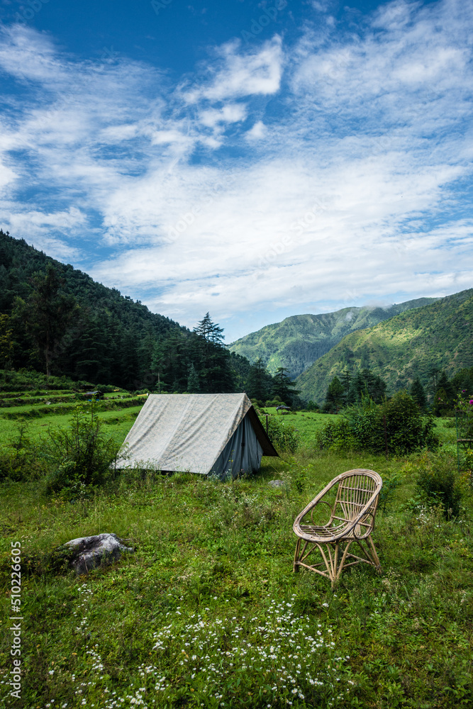 An tourist place in the meadows with a camp and a bamboo chair with mountains in the background. Uttarakhand India.