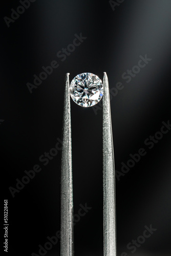 Round brilliant cut diamond with tweezers on black background