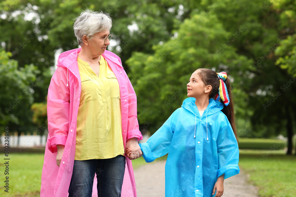 Little girl and her grandma in raincoats holding hands outdoors Little girl and her grandma in raincoats holding hands outdoors