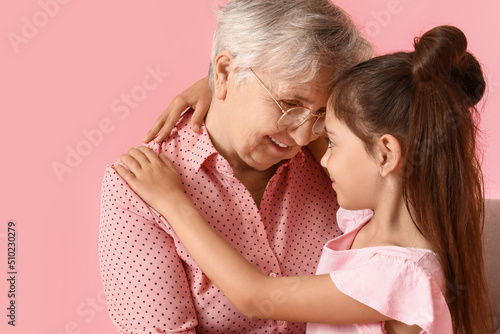 Senior woman with her little granddaughter hugging on pink background