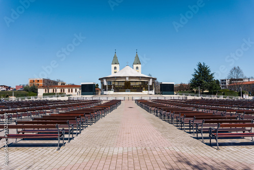 A Photograph of the exterior of the St. James church in Medjugorje with benches in the foreground