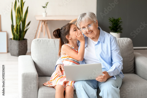 Fotografie Little girl telling to her grandma secret at home