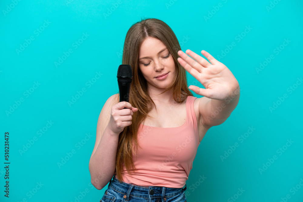 Singer caucasian woman picking up a microphone isolated on blue background making stop gesture and disappointed Singer caucasian woman picking up a microphone isolated on blue background making stop gesture and disappointed