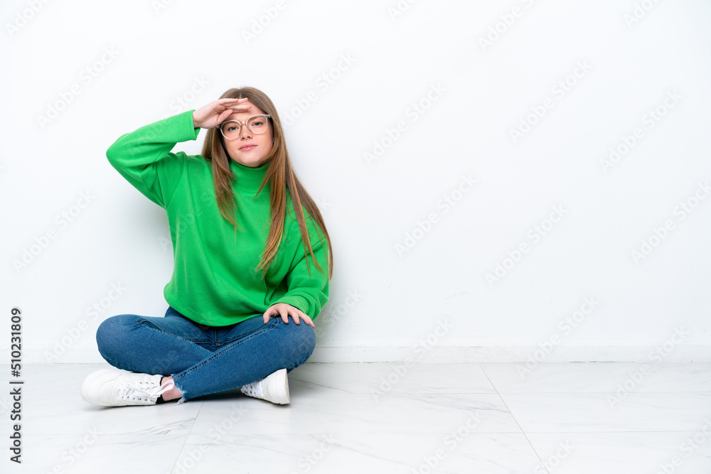 Young caucasian woman sitting on the floor isolated on white background looking far away with hand to look something Young caucasian woman sitting on the floor isolated on white background looking far away with hand to look something