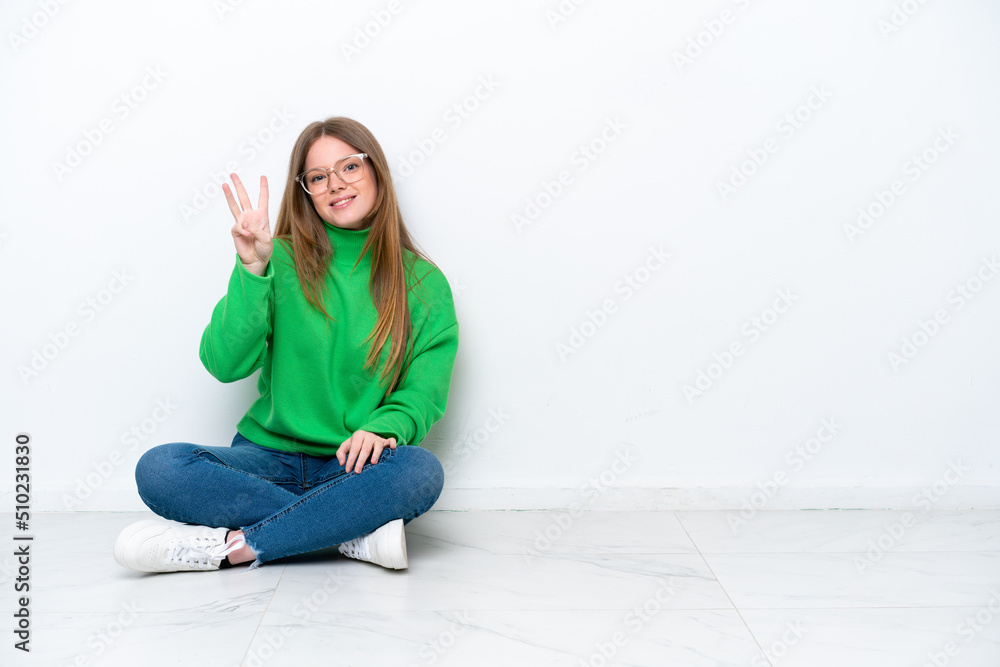 Young caucasian woman sitting on the floor isolated on white background happy and counting three with fingers Young caucasian woman sitting on the floor isolated on white background happy and counting three with fingers