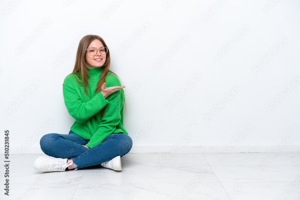 Young caucasian woman sitting on the floor isolated on white background presenting an idea while looking smiling towards Young caucasian woman sitting on the floor isolated on white background presenting an idea while looking smiling towards