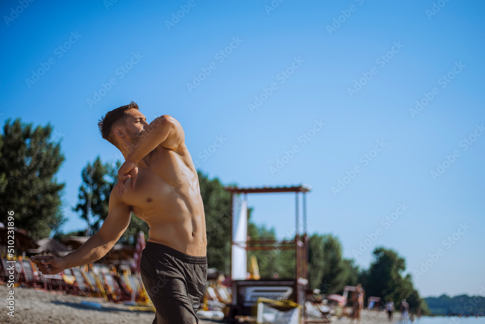 Shirtless muscular man in sunglasses on a beach.