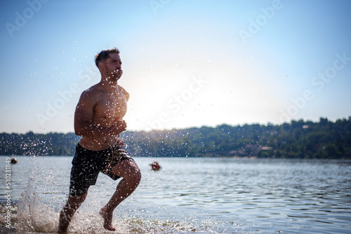 Shirtless muscular man in sunglasses on a beach.