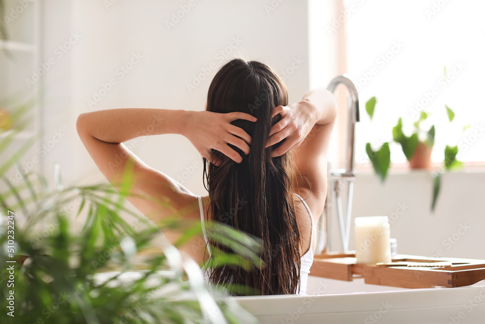 Young woman applying coconut oil onto her hair in bathroom - obrazy, fototapety, plakaty 
