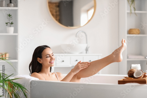 Beautiful woman applying coconut oil onto her leg in bathroom