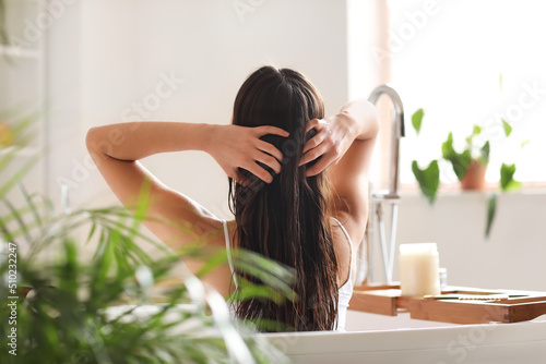 Fototapeta Young woman applying coconut oil onto her hair in bathroom