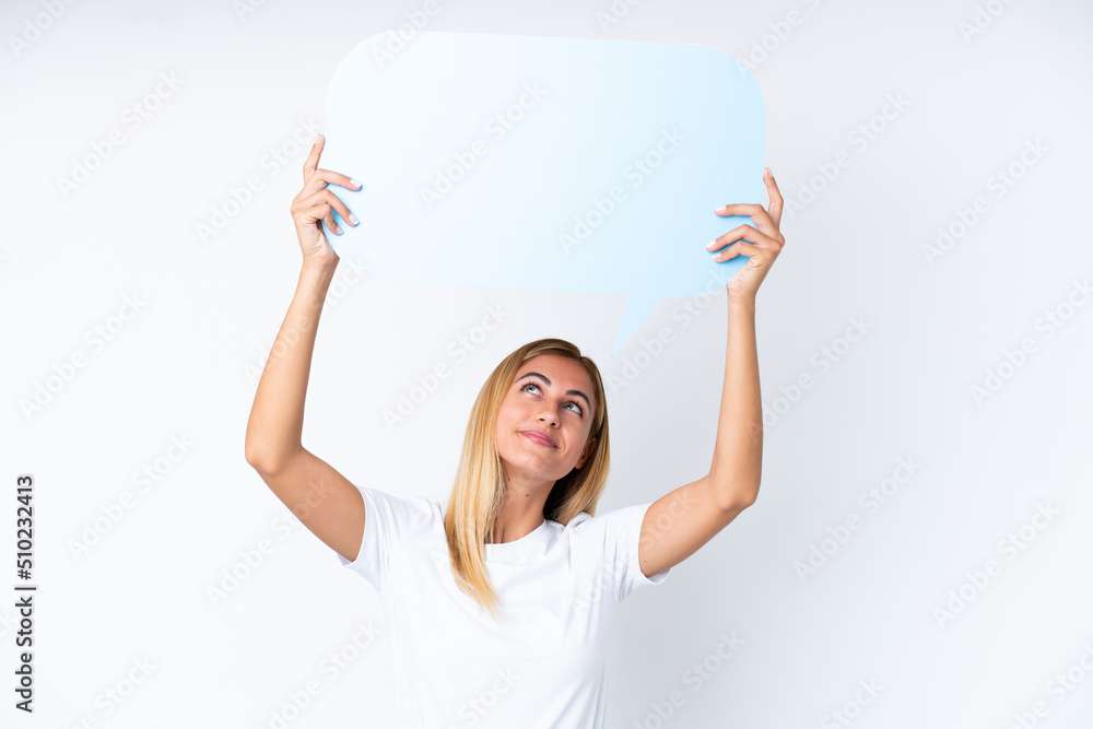 Blonde Uruguayan girl isolated on white background holding an empty speech bubble and with sad expression Blonde Uruguayan girl isolated on white background holding an empty speech bubble and with sad expression