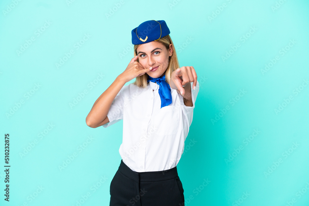 Airplane stewardess Uruguayan woman isolated on blue background making phone gesture and pointing front Airplane stewardess Uruguayan woman isolated on blue background making phone gesture and pointing front