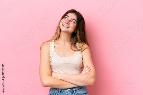 Young caucasian woman isolated on pink background looking up while smiling