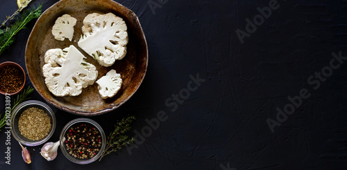 Cauliflower steak cooking. Banner. Raw parts of cauliflower lie in a frying pan. Near olive oil, various spices. Dark background. Place for text.