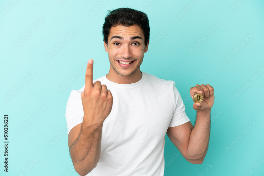 Naklejka premium Young man holding a Bitcoin over isolated blue background doing coming gesture