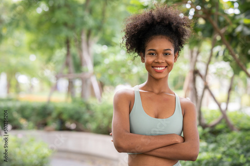 happy young sporty African american woman with curly hairstyle standing with crossed arms outdoor in the park