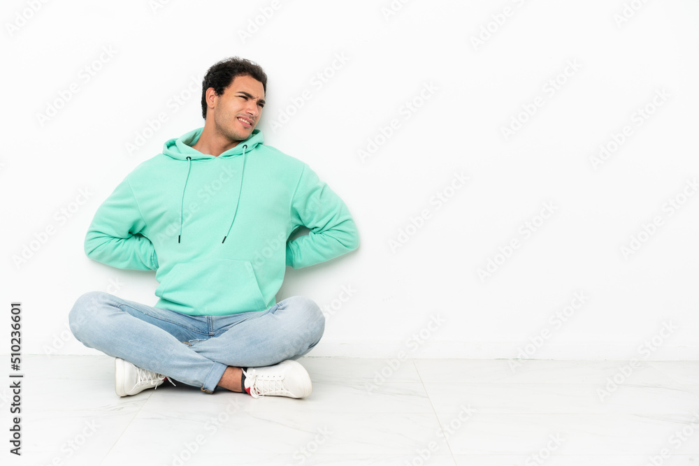 Caucasian handsome man sitting on the floor suffering from backache for having made an effort Caucasian handsome man sitting on the floor suffering from backache for having made an effort