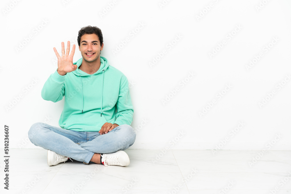 Caucasian handsome man sitting on the floor happy and counting four with fingers
